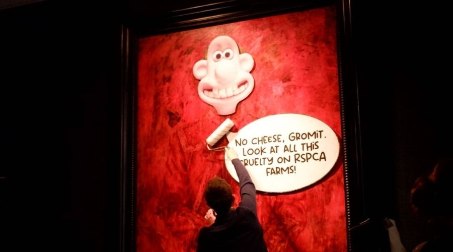 image of protestor sticking Wallace and Gromit posters to King's portrait