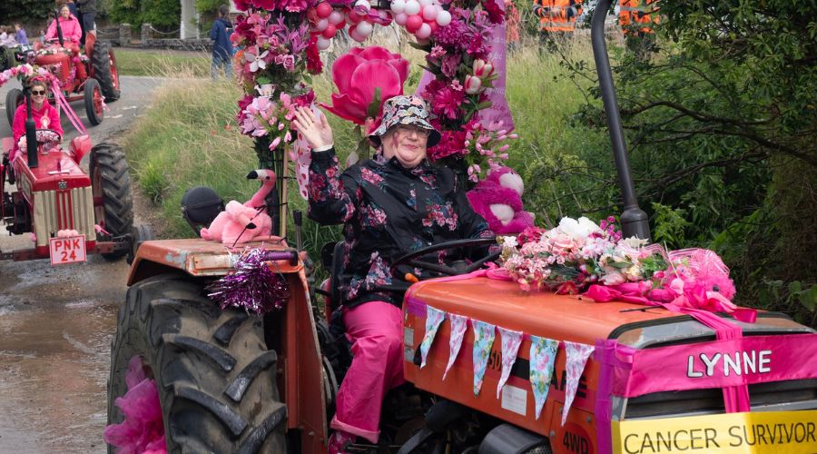 woman driving tractor with pink decorations and sign reading 'Lynne, cancer survivor', at the pink ladies tractor road run