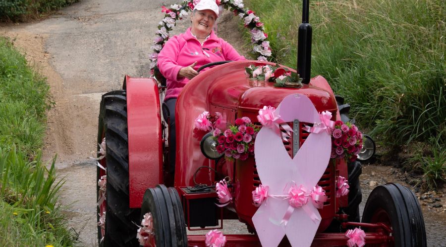 woman in pink driving a pink tractor, with breast cancer pink bow on front