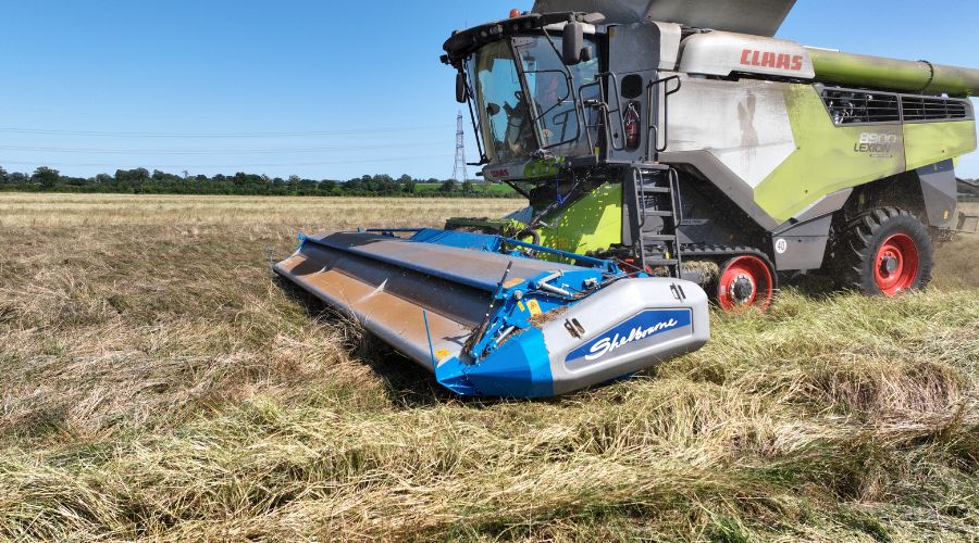 Claas Lexikon 8900 combine with a Shelbourne Reynolds stripper header attached, harvesting grass in a field - with blue sky in the background