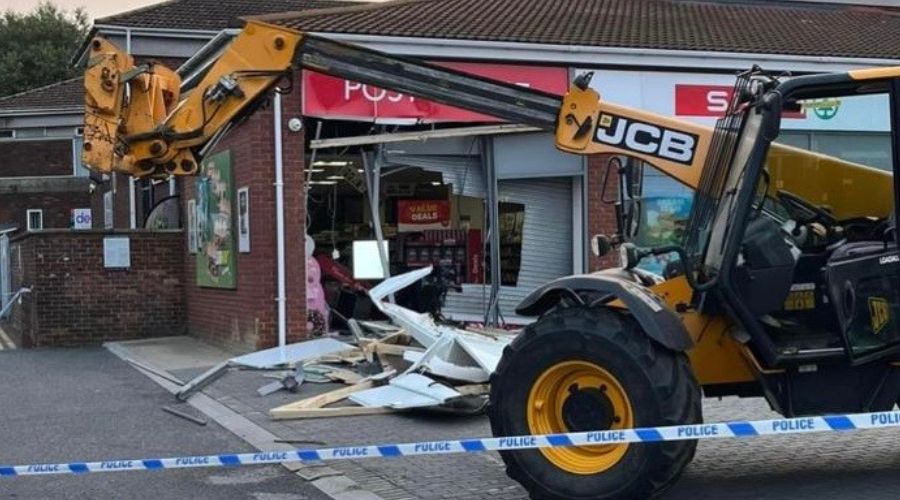 picture of a JCB telescopic loader which has smashed into the front of a post office, with police tape in the foreground