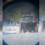 video still of a snowy field with a tractor in the centre surrounded by brown cattle