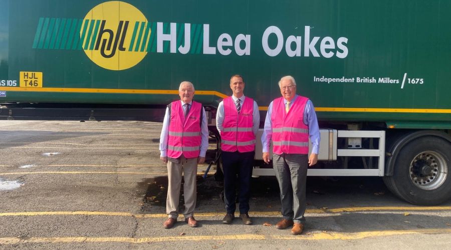 Green HJ Lea Oakes lorry, with three people standing in front of it wearing pink hi-viz jackets 