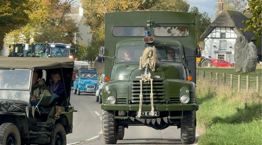 Green vintage truck with a skeleton wearing a long white wig attached to the front, driving in the tractor run