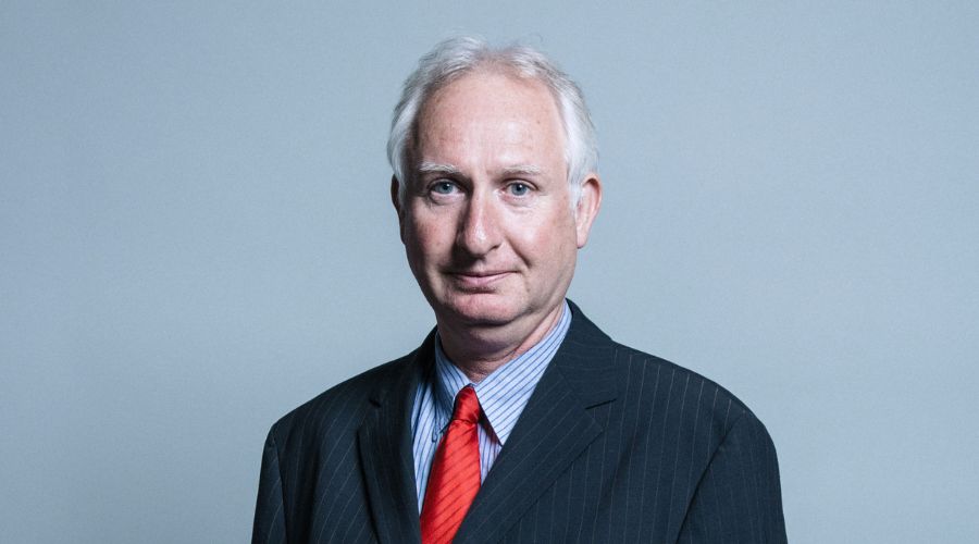 Daniel Zeichner, food security minister wearing a dark suit with red tie, on a grey background