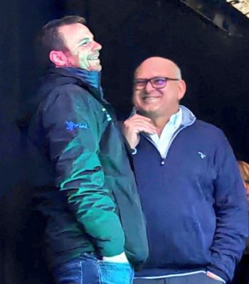 Olly Harrison and Martin Williams standing on a stage facing each other, laughing 