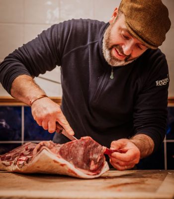 Anthony Legge, wearing a flat cap and carving a joint of beef 