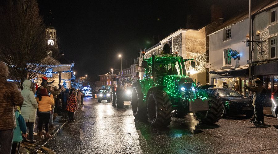 Line of people watching as a line of light up tractors drives down the road.