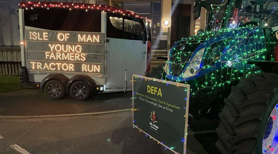 Lit up sign reading Isle of Man Young Farmers' Tractor Run, next to the front end of a tractor with green lights on it, and a sign at the front saying Department of Environment Food & Agriculture, Isle of Man Government 