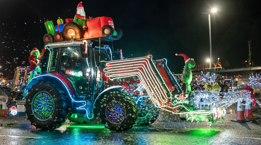 Tractor covered in lights with Grinch on the back, inflatable Santa in a sleigh with presents on top and green dragon with Santa hat on the front 