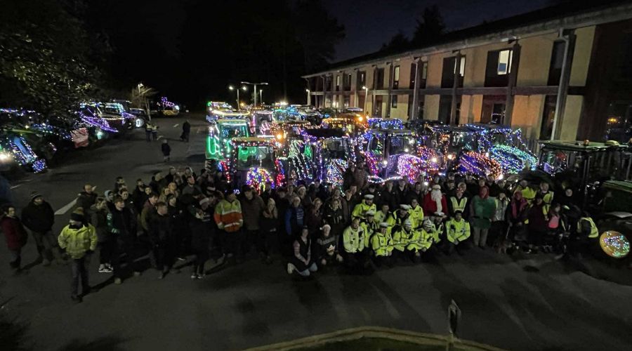 Building on the right, with lots of lit up tractors in front, and in the foreground a group of people - tractor run organisers, drivers and police wearing high vis 